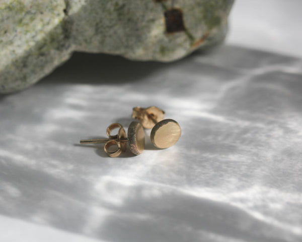 Gold stud earrings on a textured surface with a stone in the background